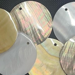 May include: A selection of iridescent, circular shell pendants in shades of gold, silver, and pearlescent. Each pendant has a small hole for threading. These pendants are suitable for jewellery making or craft projects.