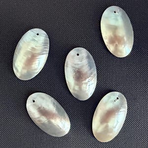 May include: Five oval-shaped mother-of-pearl pendants with an iridescent, pearlescent finish. Each pendant features a smooth, polished surface and a single small circular hole drilled near the top edge for stringing or attachment purposes.