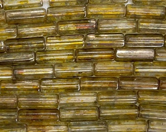 May include: A close-up of a group of glass beads. The beads are a translucent, light green color with a slightly iridescent finish. The beads are all rectangular in shape and have a slightly rounded edge.