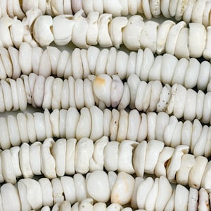May include: Close-up of multiple strands of white, irregular-shaped shell beads. The beads are strung together, creating a textured surface. Some beads have subtle pink and yellow hues. The overall aesthetic is natural and organic, suitable for jewelry making.