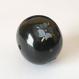 以下が含まれることがあります： 虹色の貝殻と金のアクセントで花柄が施された黒い丸いビーズ