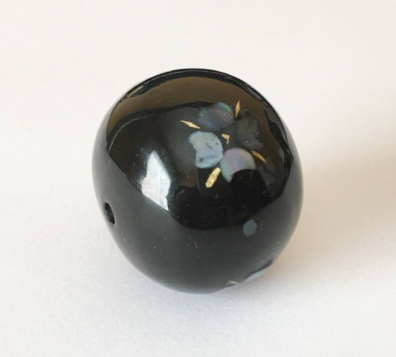 以下が含まれることがあります： 虹色の貝殻と金のアクセントで花柄が施された黒い丸いビーズ