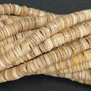 May include: Strands of beige and cream-colored shell beads. The beads are flat, disc-shaped, and strung together, creating a textured, layered appearance. The beads have a natural, organic look, with variations in color and pattern.