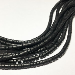 May include: A strand of black wooden beads, each bead is a small cylinder with a hole in the center. The beads are arranged in a loose, flowing pattern.