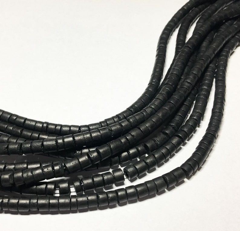 May include: A strand of black wooden beads, each bead is a small cylinder with a hole in the center. The beads are arranged in a loose, flowing pattern.