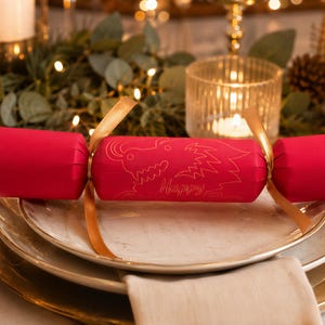 A festive Christmas table setting with a red cracker decorated with a dragon design, surrounded by greenery, candles, and other holiday decorations.