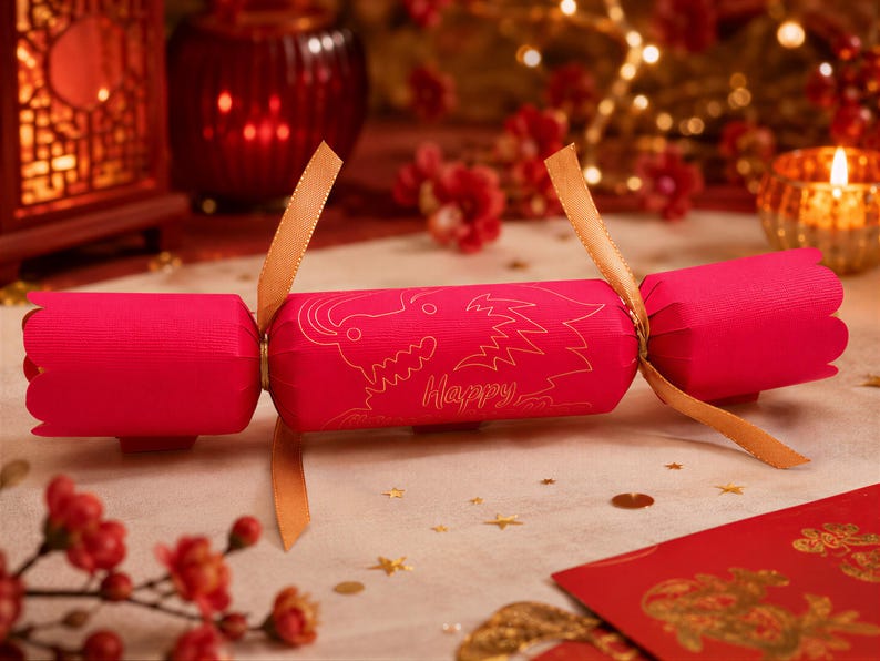 A red Chinese New Year cracker with gold accents and a dragon design sits on a table surrounded by red flowers and gold decorations.