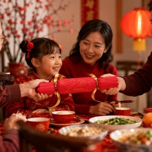 A family of three, dressed in red, is gathered around a table filled with food, smiling and enjoying a festive meal together.