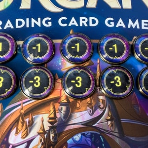 Puede incluir: Diez fichas redondas con fondo negro y borde dorado. Las fichas tienen un número blanco. Cinco fichas tienen el número -1 y cinco fichas tienen el número -3. Las fichas son para un juego de cartas coleccionables.