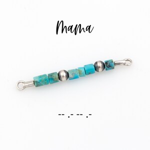 May include: A beaded bar with turquoise and silver beads. The word "Mama" is written in cursive above the bar. Below the bar is the Morse code for "Mom".