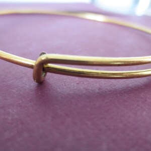 May include: A gold-toned bangle bracelet with a simple, elegant design. The bracelet is made of two thin bands of metal that are joined together at the clasp.