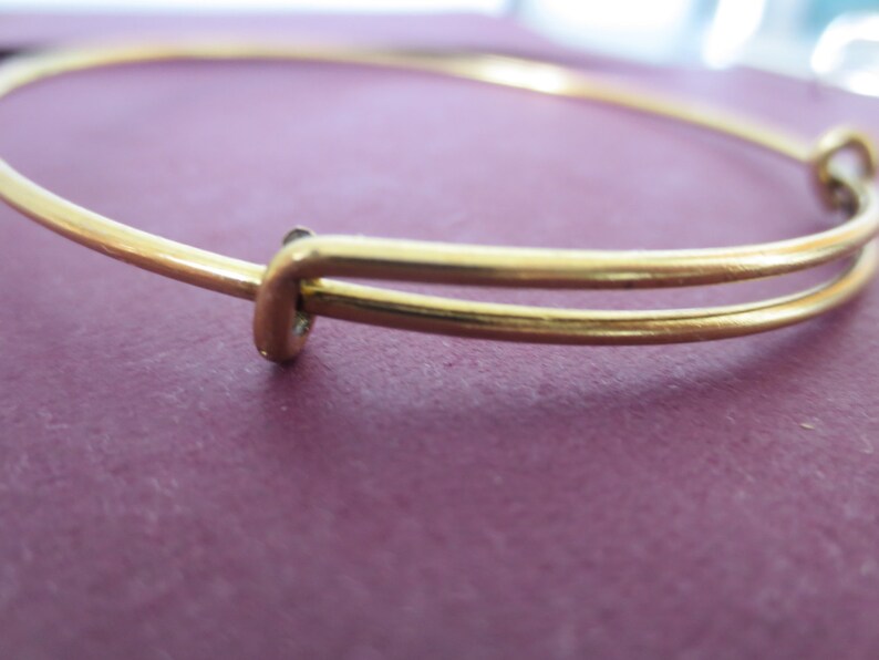 May include: A gold-toned bangle bracelet with a simple, elegant design. The bracelet is made of two thin bands of metal that are joined together at the clasp.