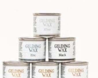 Könnte beinhalten: Ein Stapel von sechs kleinen Metalldosen mit Vergoldungswachs in verschiedenen Farben. Die Farben umfassen Silber, Zink, Schwarz, Kupfer, Gold und Bronze. Jede Dose hat ein Etikett mit Produktname und Farbe.