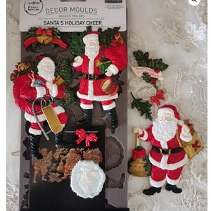 May include: A set of Christmas-themed decor molds featuring Santa Claus figures in red and white outfits. The molds include Santa with a sack, a drum, and a sleigh. The package is 5" x 10" and labeled "Santa's Holiday Cheer."