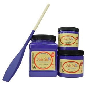 May include: An amethyst-colored paint paddle and three jars of Dixie Belle Chalk Mineral Paint. The jars are labeled with the paint color and size: 8 oz, 16 oz, and 32 oz. The paddle has a wooden handle and a purple blade.