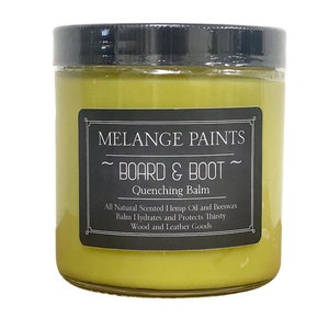 May include: A glass jar with a black lid filled with a yellow balm. The label reads "MELANGE PAINTS ~ BOARD & BOOT ~ Quenching Balm All Natural Scented Hemp Oil and Beeswax Balm Hydrates and Protects Thirsty Wood and Leather Goods"