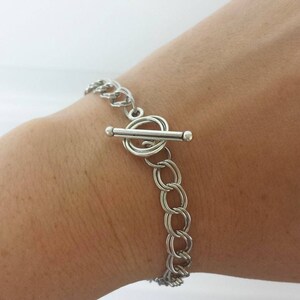 May include: A silver chain bracelet with a toggle clasp. The bracelet is made of multiple linked circles.