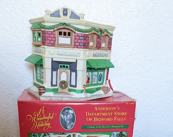 May include: A white ceramic model of Anderson's Department Store from the movie "It's a Wonderful Life". The model is lit up and has a green awning with the words "Anderson's" on it. The box is red and has the title "A Wonderful Holiday" on it.