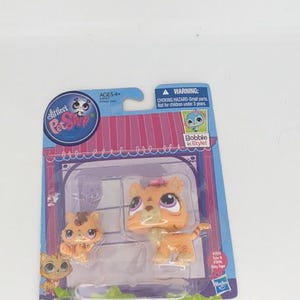 May include: A package of Littlest Pet Shop toys featuring two orange tabby cat figures. The packaging includes the brand logo, age recommendation, and a warning about small parts. The toys are designed with bobbling heads.