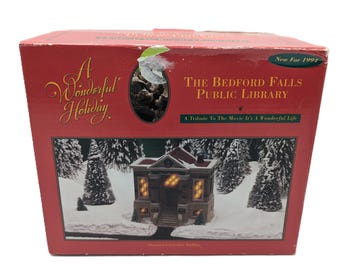 May include: A red cardboard box for a collectible porcelain building titled The Bedford Falls Public Library, A Tribute To The Movie It's A Wonderful Life. The box features a graphic of a lit building in a snowy landscape and text New For 1994.