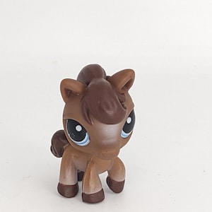 Puede incluir: Figura de caballo de juguete marrón con crin y cola marrón oscuro. El caballo tiene grandes ojos azules con reflejos blancos. El juguete es de plástico y tiene un acabado brillante. El caballo está de pie sobre sus cuatro patas.
