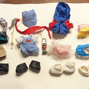 Puede incluir: Colección de ropa y accesorios de muñecas en miniatura, que incluye una chaqueta azul con detalles rojos, petos, pantalones cortos, sombreros, zapatos y una caña de pescar. Los artículos son de varios colores y estilos.