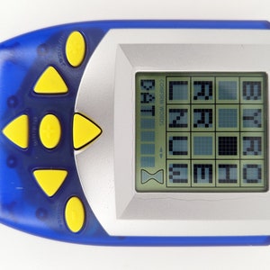 Peut inclure: Un jeu électronique portable bleu et argent avec des boutons jaunes. L'écran affiche le mot "BOGGLE" et une grille de lettres. Le jeu est conçu pour aider les joueurs à trouver des mots dans la grille.