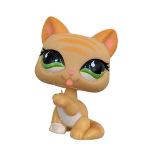 Puede incluir: Una figura de gato marrón y naranja con ojos grandes y expresivos. El gato tiene ojos verdes y negros, rayas naranjas y una lengua rosa que sobresale. La figura es un juguete coleccionable.