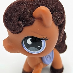 May include: A brown toy pony with a dark brown mane and tail. The pony has large blue eyes with black eyelashes and a light blue saddle. The toy is made of plastic and has a smooth finish.
