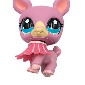 May include: A pink llama figurine with large, expressive eyes, a light yellow nose, and a pink skirt. The toy has large ears with pink inner ears and is posed on a white background.