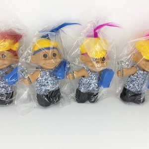 Puede incluir: Cuatro muñecos troll que llevan cascos amarillos y monos azules. Cada muñeco sostiene una llave inglesa y una caja de herramientas azul. Los muñecos están empaquetados en bolsas de plástico transparentes.