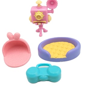 Puede incluir: Una colección de accesorios de juguete coloridos, que incluyen una cámara rosa con un flash en forma de flor, un bolso rosa, una cama para mascotas azul y una radio turquesa. Estos juguetes están diseñados para el juego imaginativo.