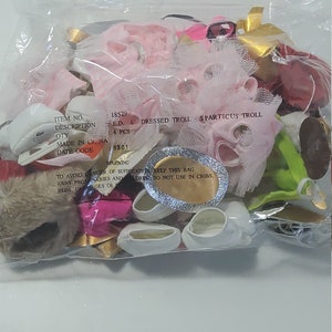 May include: A plastic bag filled with pink, white and green doll clothes. The bag includes a pink dress, a white tutu, a green skirt and white shoes. The bag also includes a tag with the text "E.D. 6 DRESSED TROLL SPARTICUS TROLL 4 PCS 9301 WARNING TO AVOID DANGER OF SUFFOCATION, KEEP THIS BAG AWAY FROM BABIES AND CHILDREN DO NOT USE IN CRIBS."