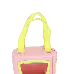 May include: A pink plastic toy oven with yellow handles and a clear window. The oven has a flower design on the front.