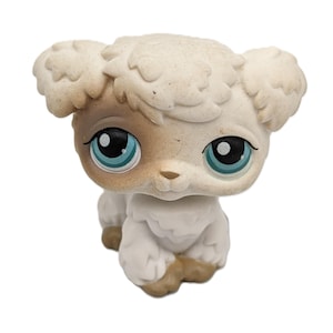 Puede incluir: Figura de oveja de juguete de color crema con detalles en marrón claro en la cara y las patas. La oveja tiene grandes ojos azules y está en posición sentada. Objeto de colección.