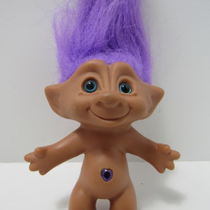 Könnte beinhalten: Eine Trollpuppe mit lila Haaren, blauen Augen und einem lila Herz auf dem Bauch.
