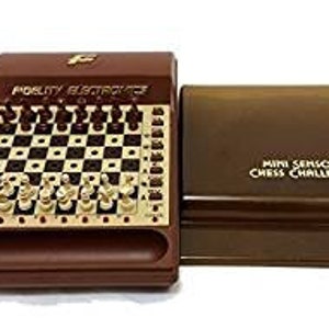 May include: A brown electronic chessboard with a clear plastic cover. The chessboard has a white and brown checkered pattern and gold-coloured chess pieces. The text "Mini Sensory Chess Challenger" is printed on the cover.