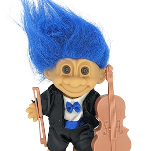 May include: A blue-haired troll doll wearing a black tuxedo and a blue bow tie, holding a brown cello.