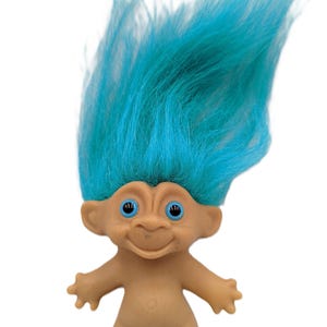 Puede incluir: Una muñeca troll vintage con un cuerpo bronceado, brazos extendidos y una cara sonriente. La muñeca tiene cabello azul brillante, erguido y puntiagudo y ojos azules. Un juguete clásico de la década de 1960.