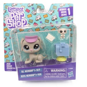 Puede incluir: Un set de juguetes Littlest Pet Shop que incluye una figura de perro gris con visera rosa, un cachorro blanco más pequeño, un sobre blanco y un buzón azul. El empaque muestra el texto Littlest Pet Shop, Series 1, Bill Weimaran 1-107 y Bertie Weimaran 1-108.