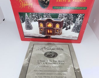 May include: A red box with a white and gold logo that says "A Wonderful Holiday." The box features a picture of a building with lights on and the text "The Bedford Falls Trust & Savings." The box is a tribute to the movie "It's a Wonderful Life."