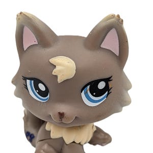 May include: A brown and tan toy cat figurine with blue eyes and a cream-colored patch on its forehead. The cat has a cream-colored ruff and pink inner ears. The toy is a collectible item.
