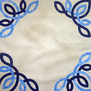 May include: A white fabric square with four blue and black intertwined leaf designs in each corner.