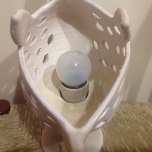 Op de afbeelding: Witte keramische lampenvoet met een gloeilamp erin. De voet heeft een uniek ontwerp met uitsparingen en een afgeronde vorm.