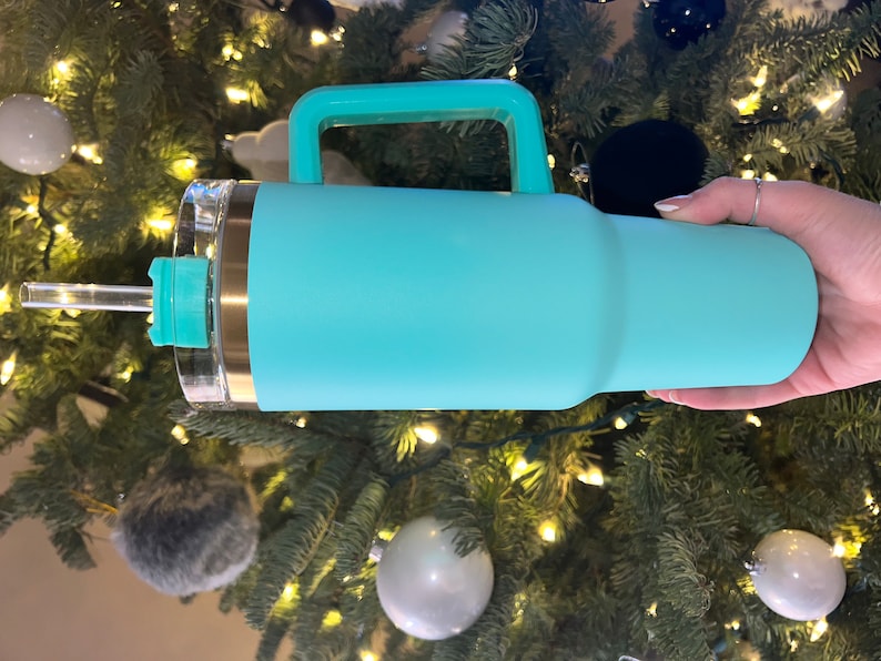 May include: A turquoise stainless steel travel mug with a handle and a clear lid. The mug has a gold band around the top and a clear straw.