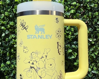 May include: Yellow Stanley tumbler with a white lid and straw. The tumbler features a handle and is decorated with Winnie the Pooh characters, bees, butterflies, and floral designs. The Stanley logo is visible.