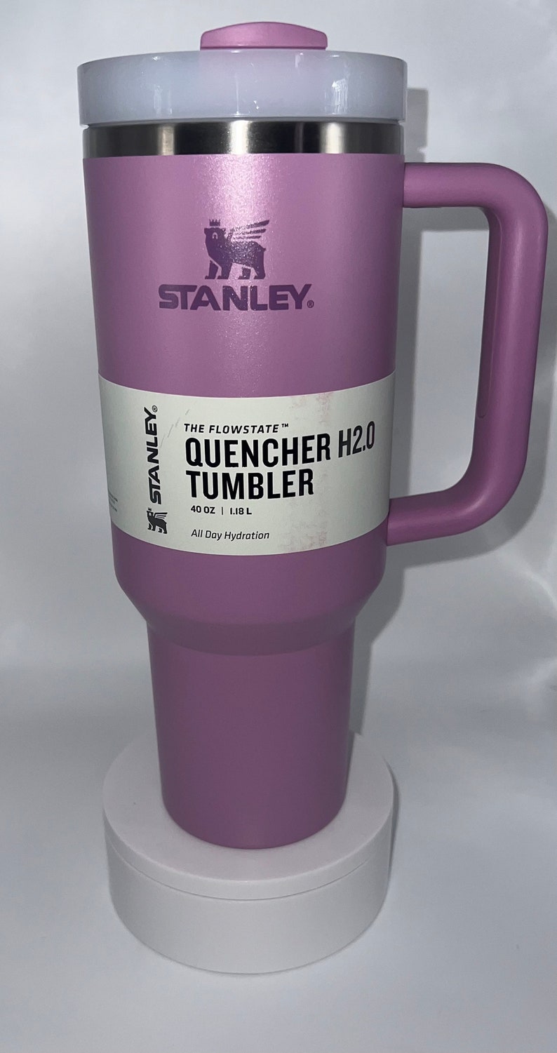 May include: A purple Stanley Quencher H2.0 Tumbler with a white lid and a black bear logo. The tumbler is 40 ounces or 1.18 liters and says "All Day Hydration".