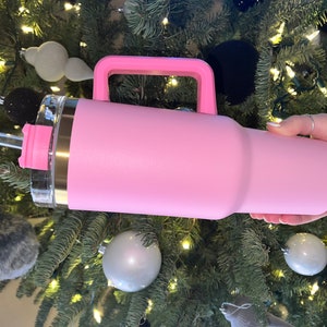 May include: A pink stainless steel travel mug with a handle and a lid. The mug has a straw and a straw lid.