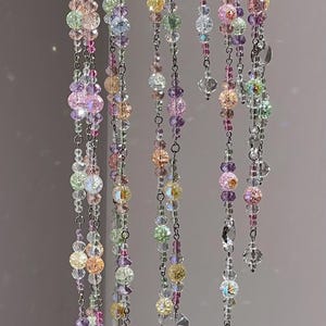 May include: A hanging mobile featuring multiple vertical strands of silver-toned metal chains adorned with a variety of multicolored glass beads. The beads include clear, pink, yellow, purple, and light green spheres with crackled and faceted textures.