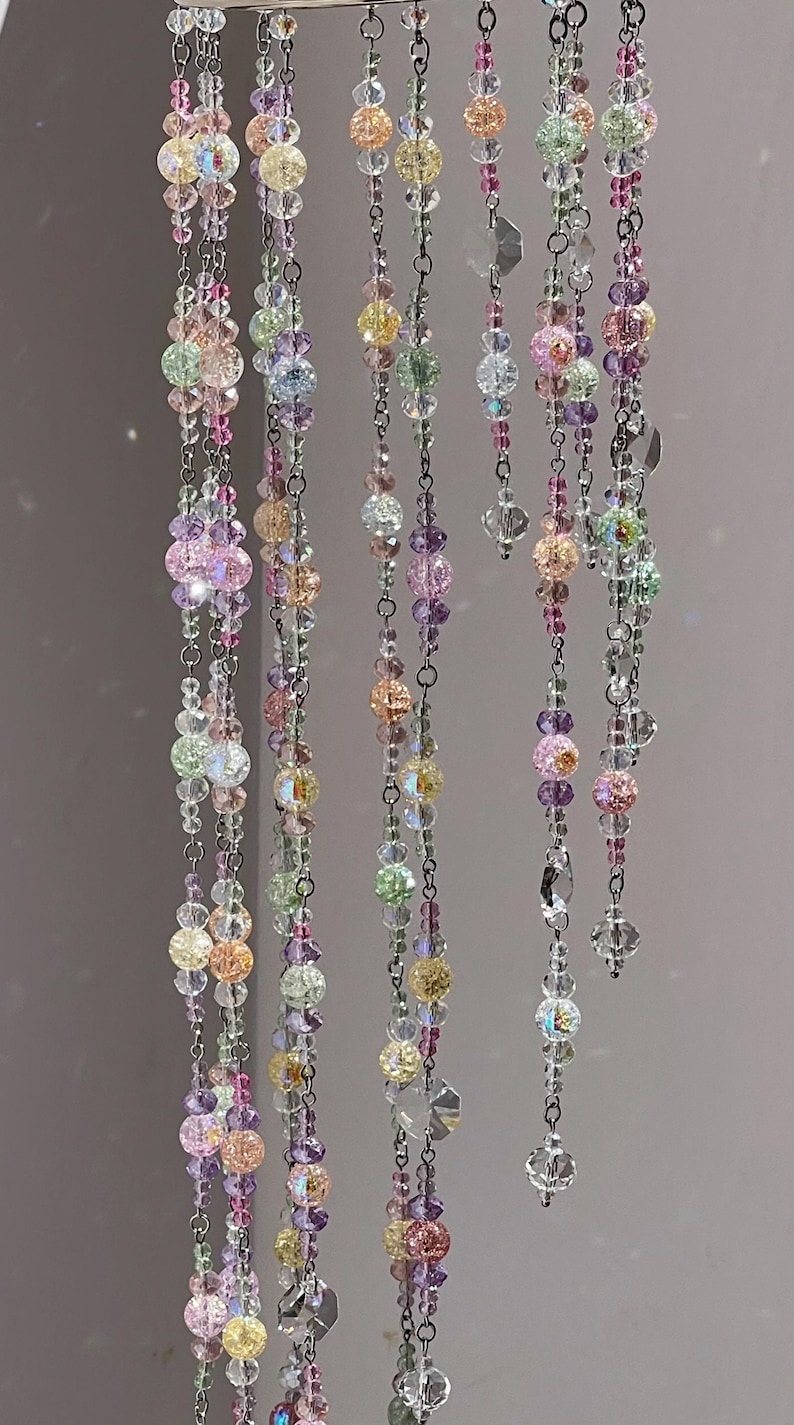 May include: A hanging mobile featuring multiple vertical strands of silver-toned metal chains adorned with a variety of multicolored glass beads. The beads include clear, pink, yellow, purple, and light green spheres with crackled and faceted textures.